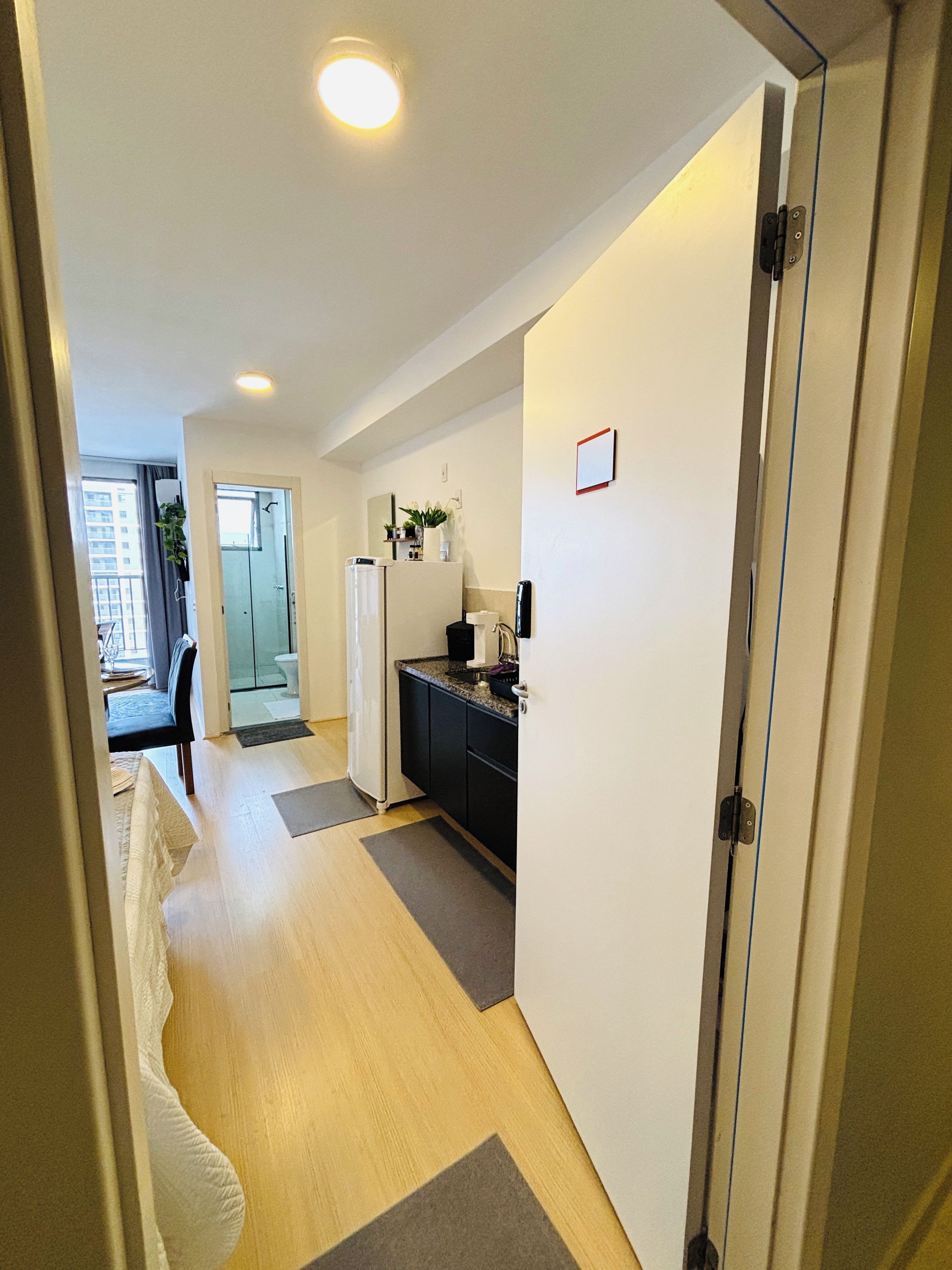 A hallway with a kitchen area, a refrigerator, and a door leading to a bathroom.
