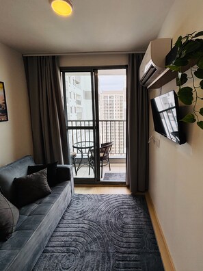 A compact living space with a sofa, a small table, and a TV mounted on the wall. - Pateo Rio Stay, Porto Maravilha, Rio de Janeiro. (Rio de Janeiro)