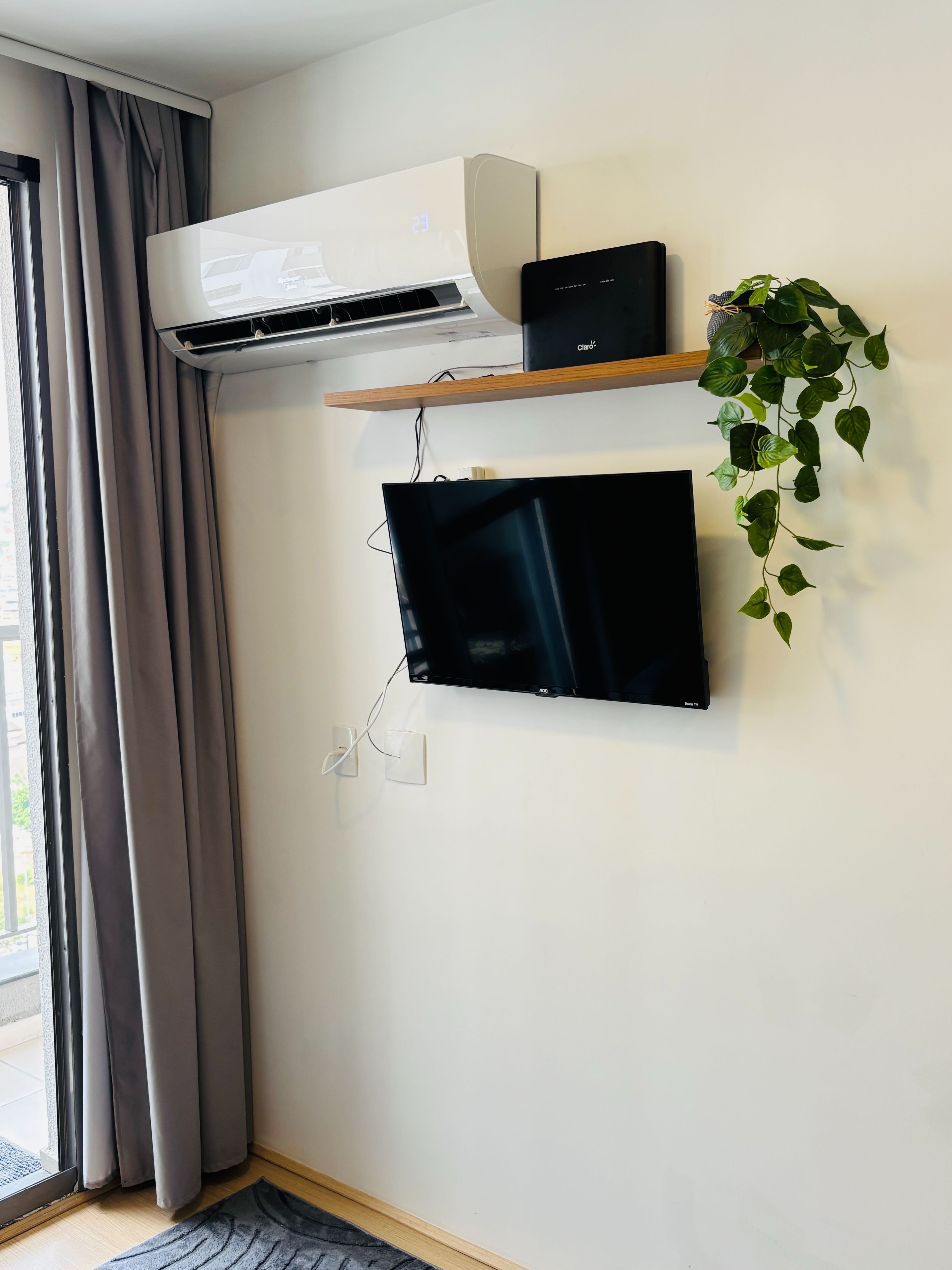 A room with a mounted TV, an air conditioning unit, a power strip, and a potted plant.