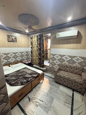 A bedroom with a bed, a sofa, a ceiling fan, an air conditioning unit, and patterned walls.