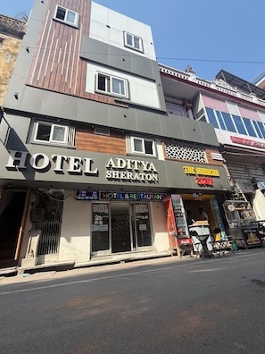 A hotel named 'Aditya Sheraton' with a sign indicating 2 and 4 bed options, Wi-Fi availability, and a Coca-Cola refrigerator outside.