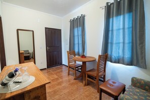 Ein Zimmer mit einem Holztisch, zwei Stühlen, einem kleinen runden Tisch mit einem einzelnen Stuhl, einer Couch, einem Spiegel und einer Tür.