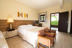 Ein Hotelzimmer mit Bett, Nachttisch, Lampe, Stuhl und einem Fenster mit Vorhängen.