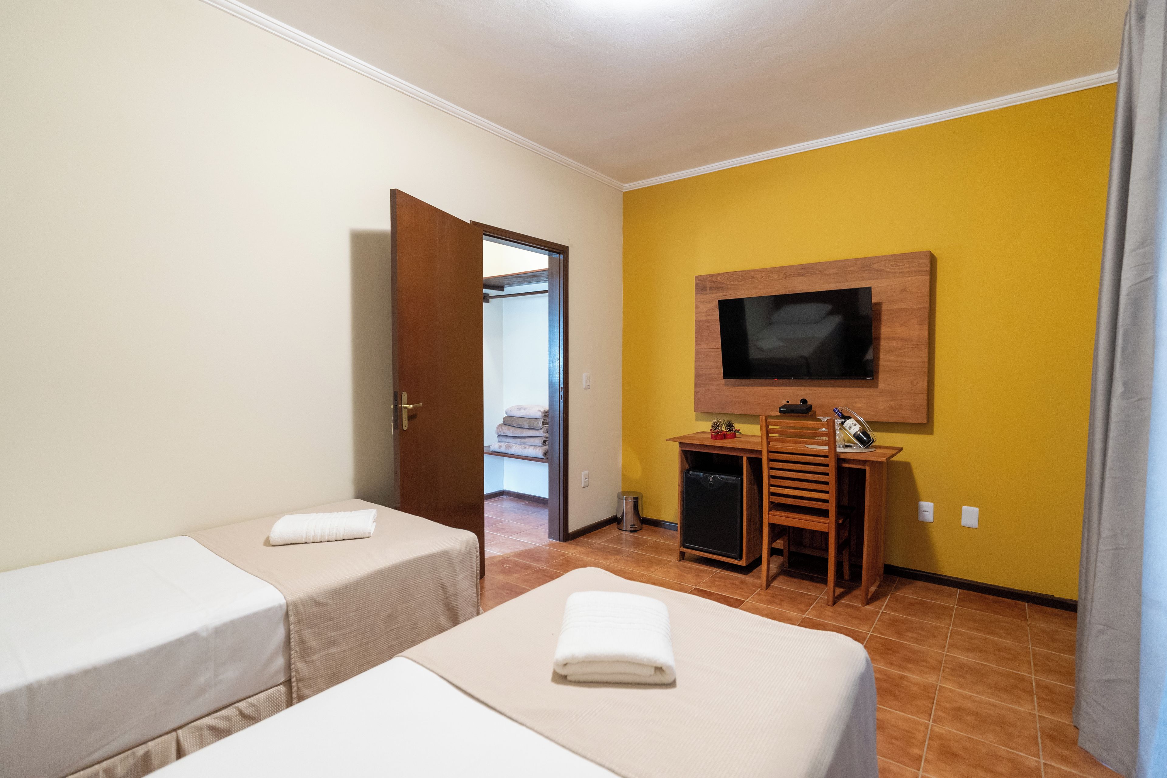 Ein Hotelzimmer mit zwei Einzelbetten, einem an der Wand montierten Fernseher, einem Schreibtisch mit Stuhl und einer Tür zu einem Badezimmer.