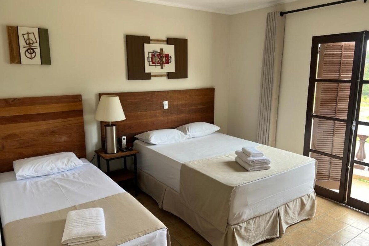 Ein Hotelzimmer mit zwei Betten, einem Nachttisch, einer Lampe und einer Tür zu einem Außenbereich.
