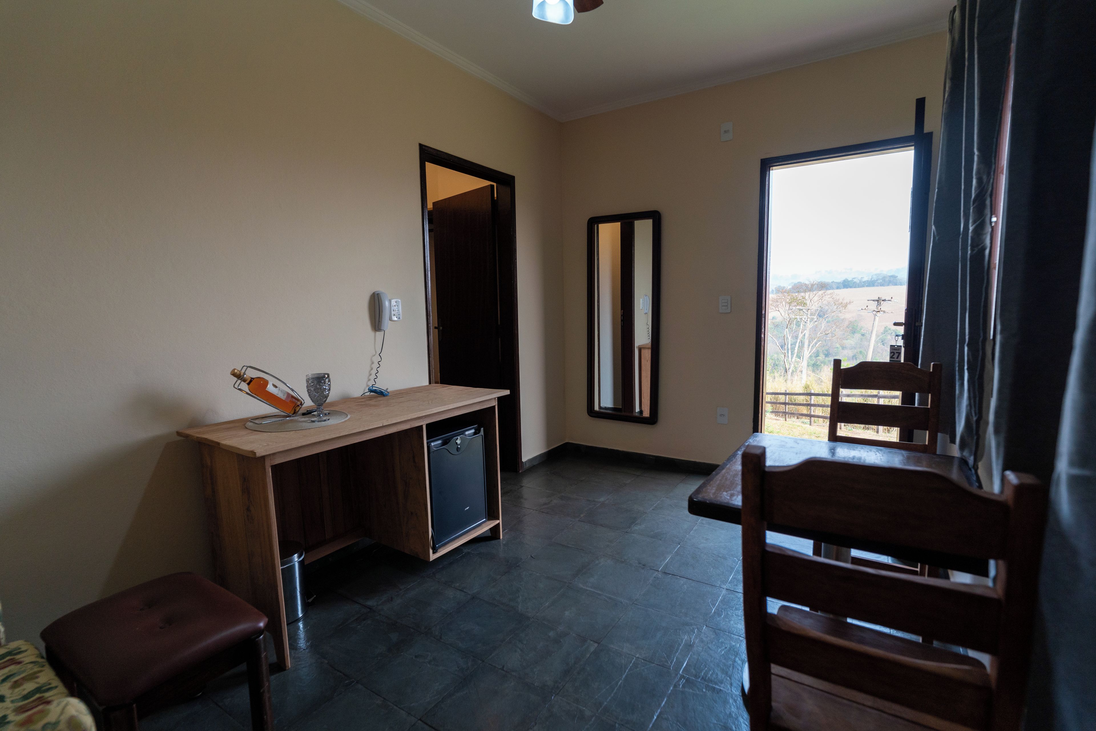 Une pièce avec un bureau en bois, une petite poubelle, une chaise et une vue par la fenêtre.