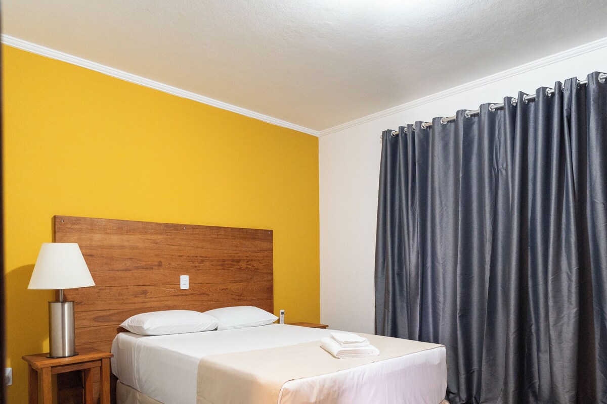 Ein Hotelzimmer mit einem Bett, einem Nachttisch, einer Lampe und einem Vorhang.