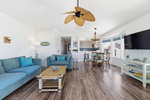 A modern living room with a sofa, coffee table, and dining area with chairs. - 🌊La Mer | 3Br Oceanfront Condo with Shared Beach Walkover🧜‍♀️ (Carolina Beach)