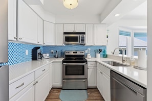 A modern kitchen with white cabinets, a microwave, stove, and dishwasher. - 🌊La Mer | 3Br Oceanfront Condo with Shared Beach Walkover🧜‍♀️ (Carolina Beach)