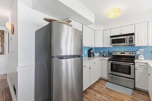 Cozinha moderna com armários brancos, eletrodomésticos de aço inoxidável e um backsplash com padrão azul.