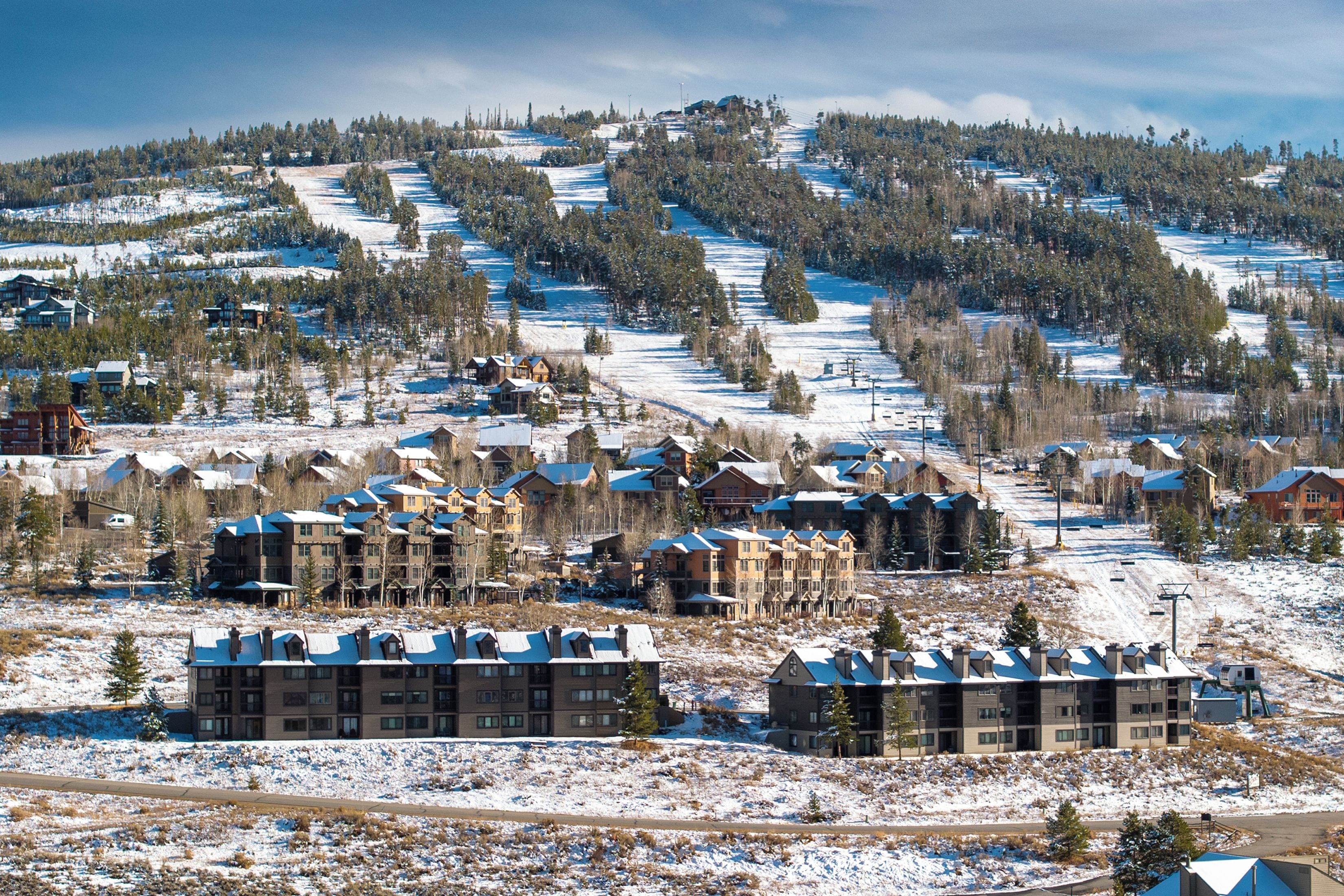 A ski resort with multiple buildings, including a large lodge and several smaller structures, surrounded by snow-covered terrain and trees.