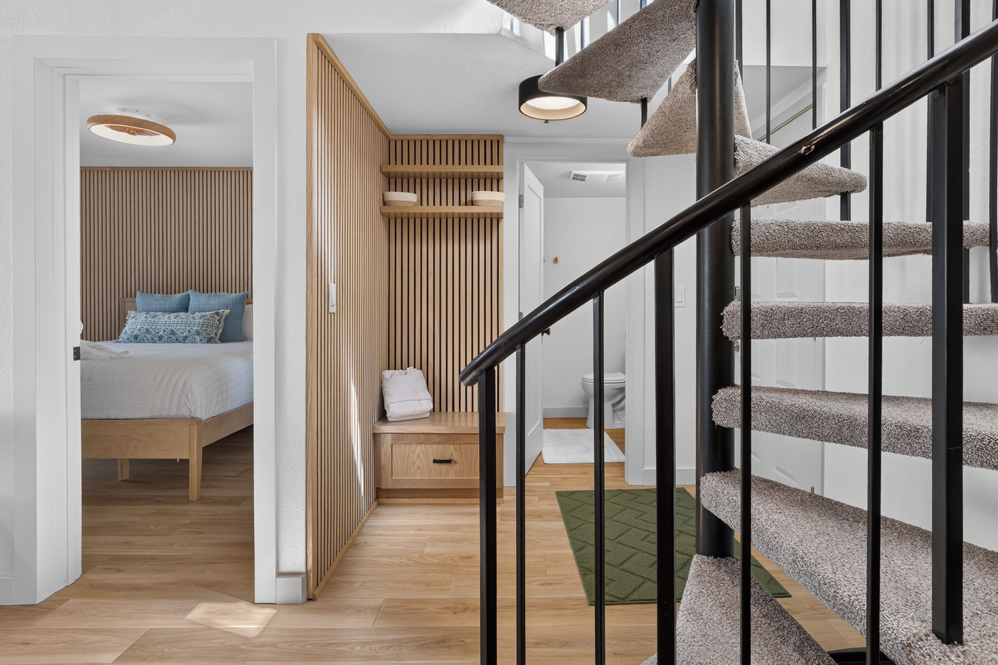 Ein modernes Interieur mit Holzboden, einem Bett mit blauer Bettwäsche, einer Treppe mit schwarzen Geländern und einer Holzwand mit vertikalen Lamellen.