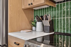 Una cocina con encimera blanca, horno de acero inoxidable, armarios de madera y salpicadero de azulejos verdes.