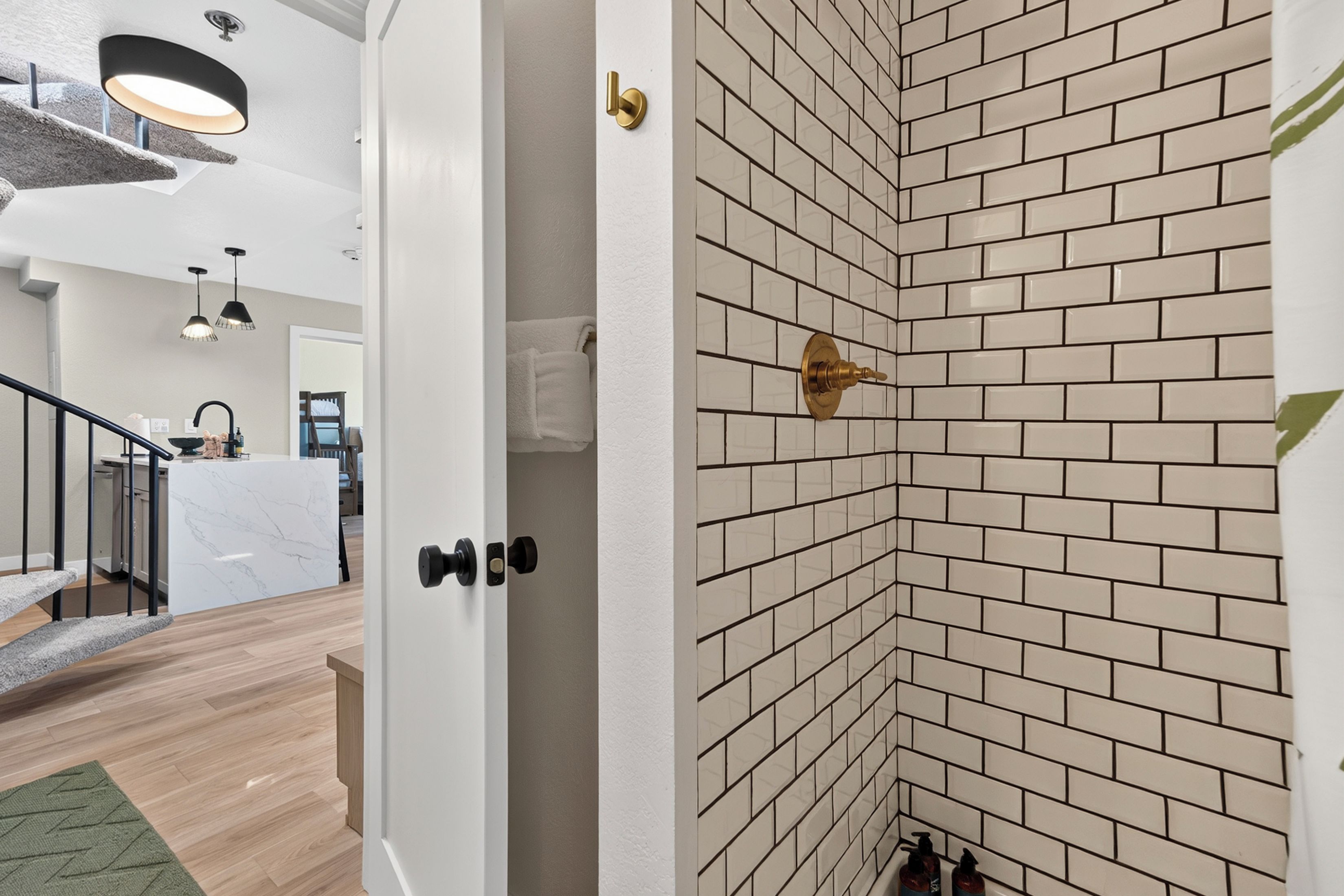 A modern interior with a kitchen area, a staircase, and a corner with a brick-patterned wall.