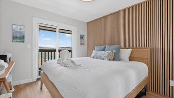 A bedroom with a large bed, a wooden slatted wall, a desk with a chair, and a view through a glass door.