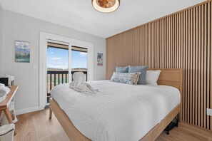A bedroom with a large bed, a wooden slatted wall, a desk with a chair, and a view through a glass door. - Why You’ll Love this Colorado Escape • Ski-in/ski-out access adjacent to the Gra (Granby)