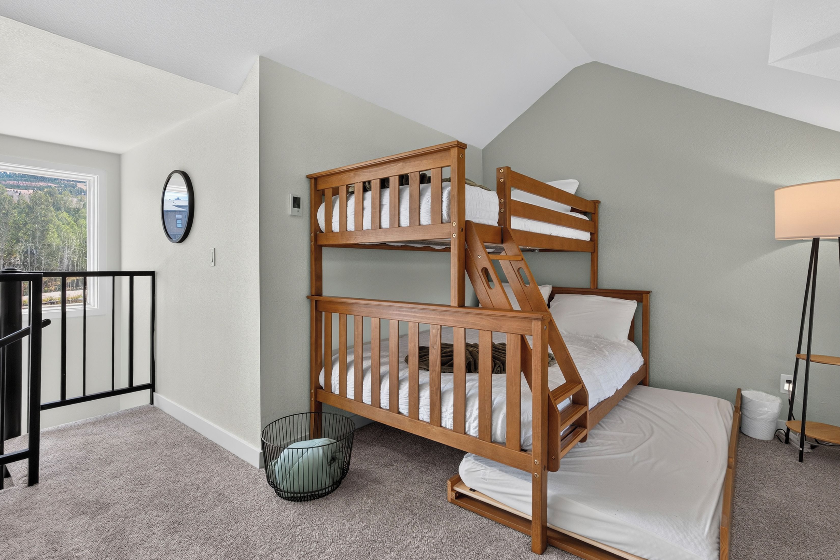 A room with a bunk bed, a small round mirror, a lamp, and a view of the outdoors.