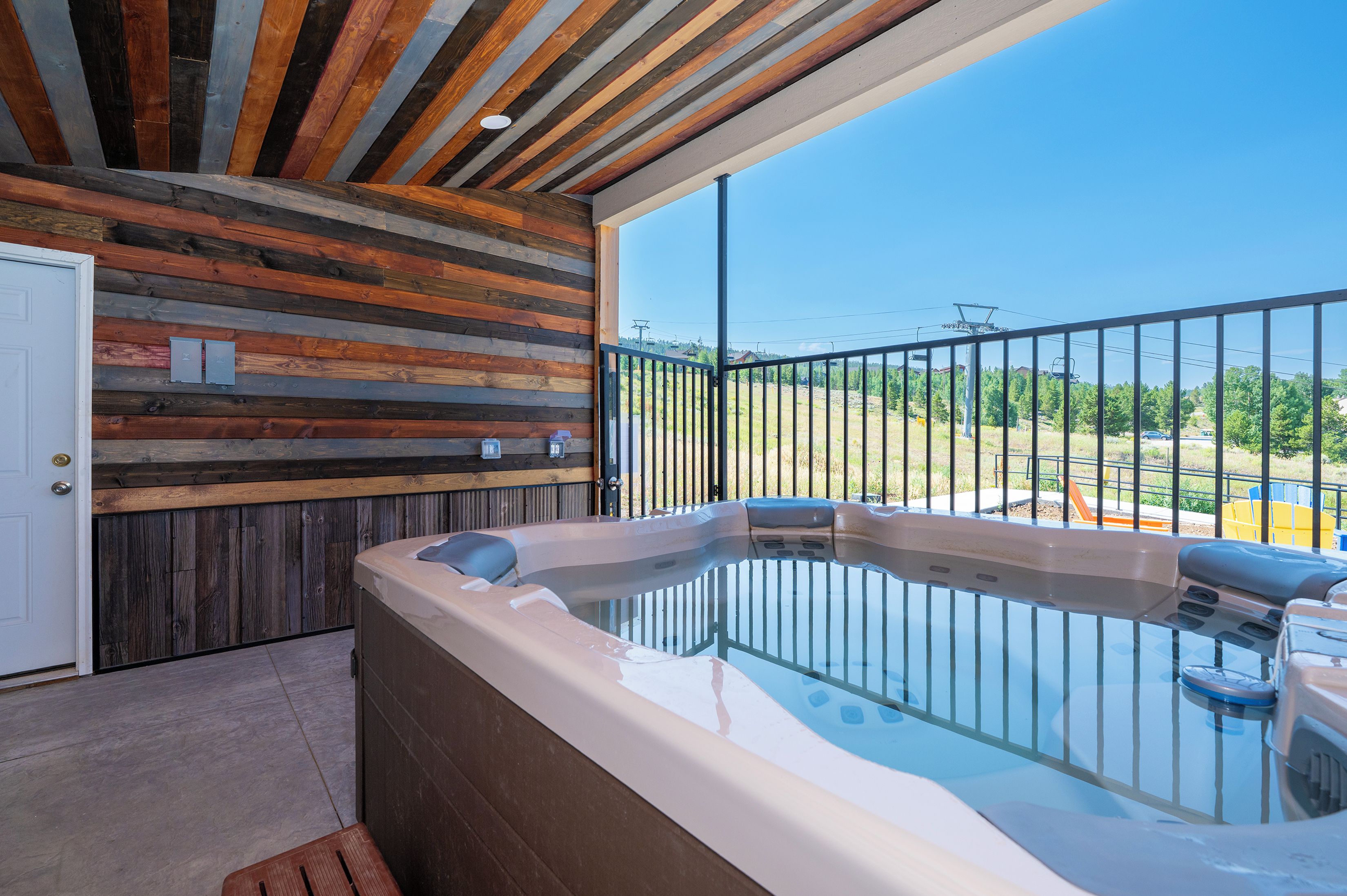 A hot tub with a wooden wall and a balcony with a metal railing.
