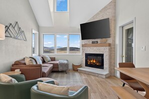 Una sala moderna con chimenea, sofá, televisor y vista al exterior.