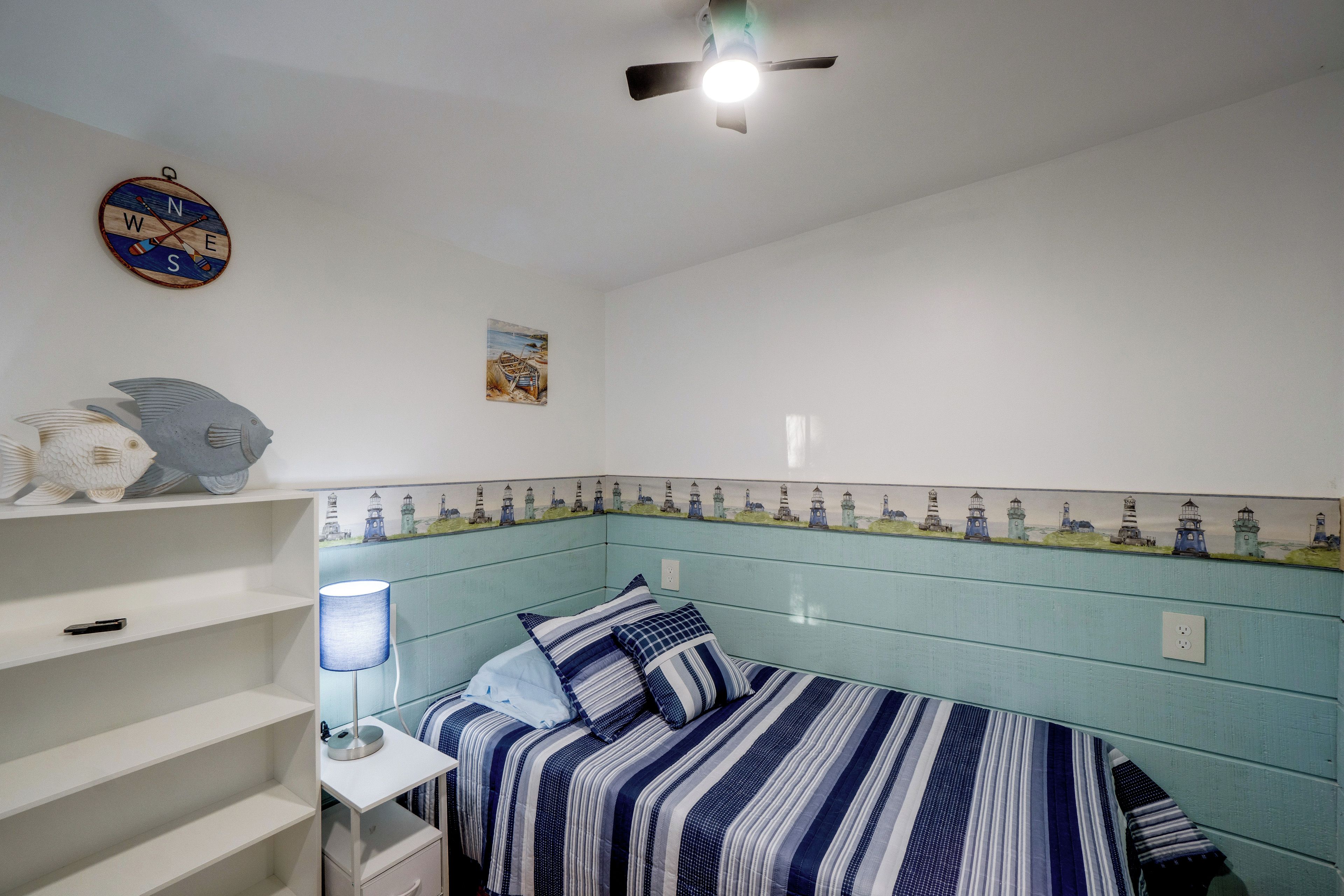 A bedroom with a bed, a shelf with decorative items, a wall clock, and a ceiling fan.