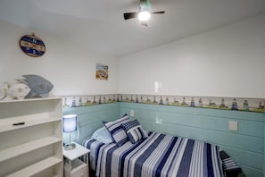 A bedroom with a bed, a shelf with decorative items, a wall clock, and a ceiling fan. - Walk to Lake Ontario! 'minnow Cottage' (Kent)