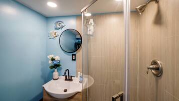 A bathroom with a sink, mirror, and shower.