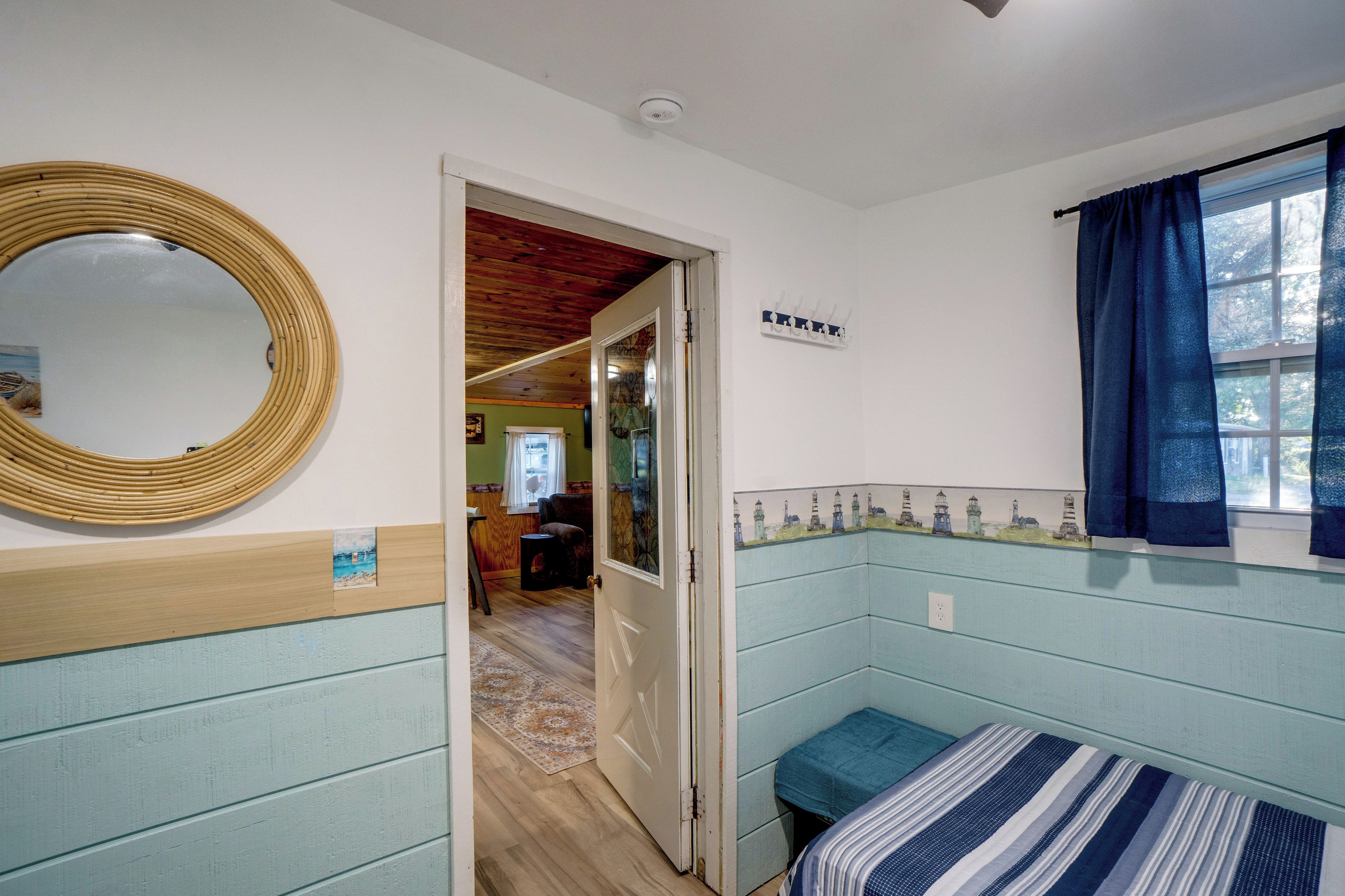 Una habitación con cama, un espejo, una ventana con cortinas y una puerta que da a otra habitación.