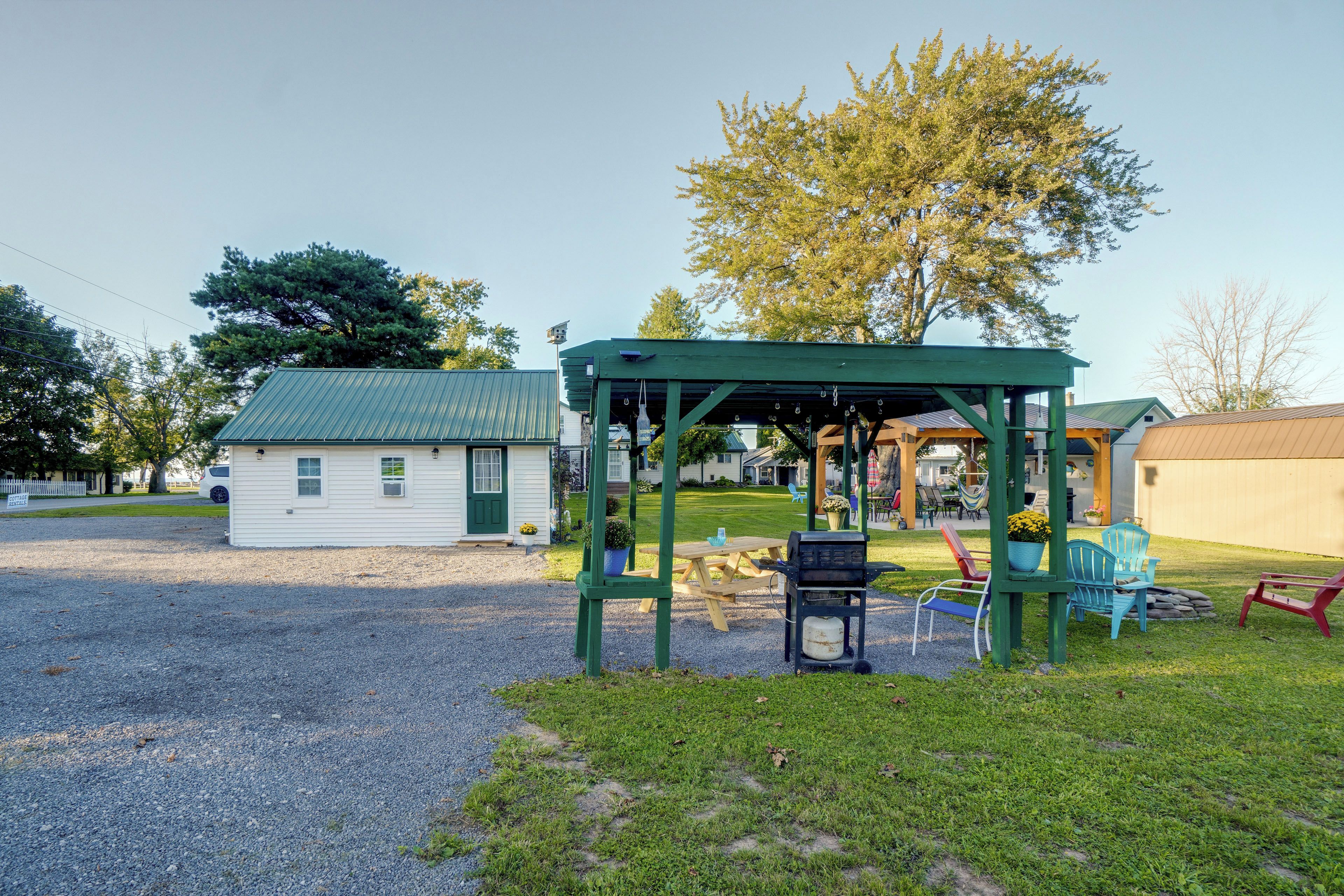 A covered outdoor seating area with a grill, picnic table, and chairs.