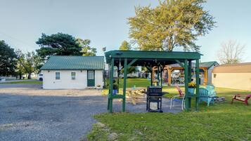 A covered outdoor seating area with a grill, picnic table, and chairs.