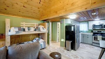 A cozy cabin interior with a bunk bed, a sofa, a kitchen with modern appliances, and a wooden ceiling.