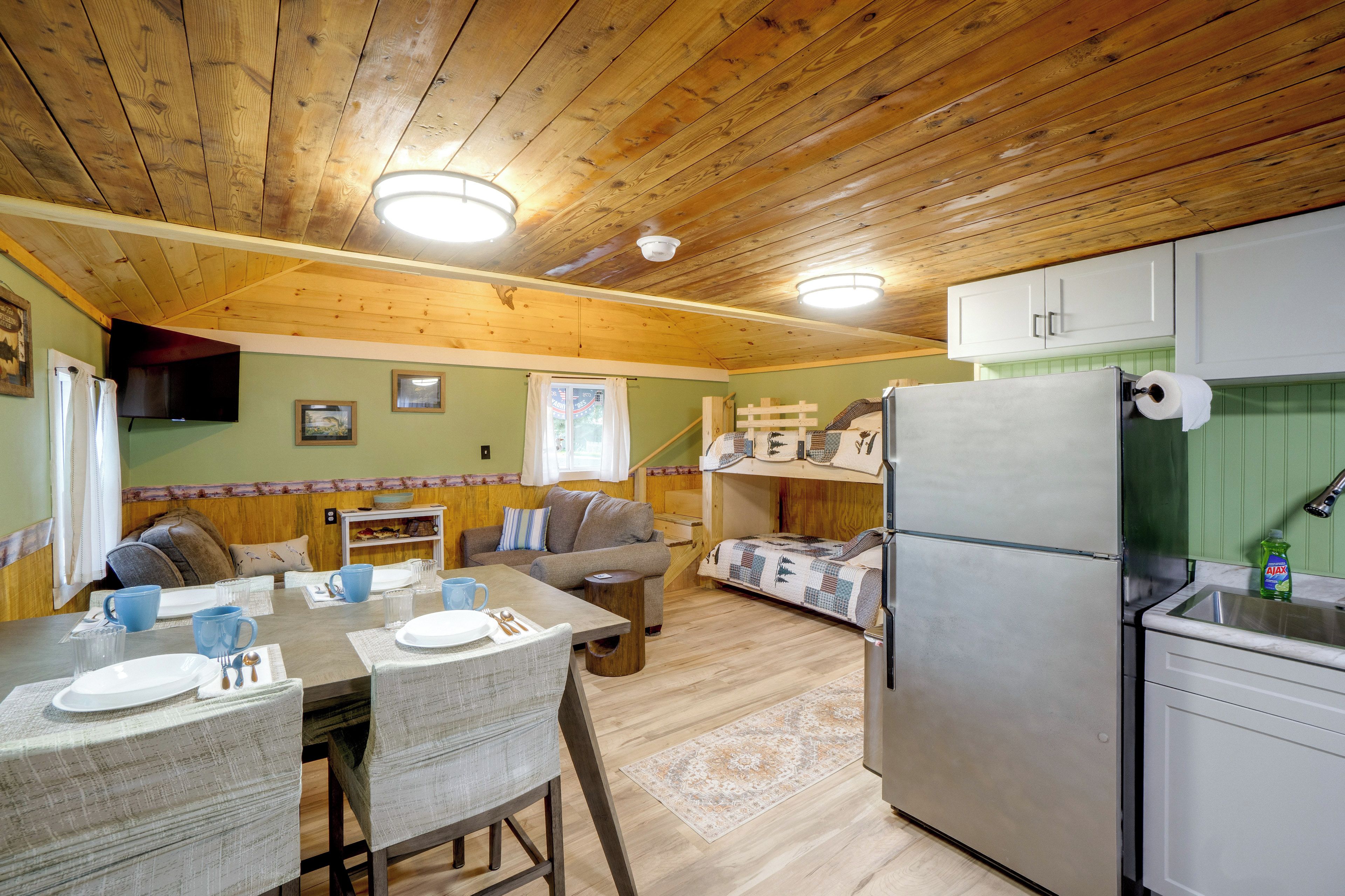 A compact kitchen with a refrigerator, a dining table with chairs, and a sofa.