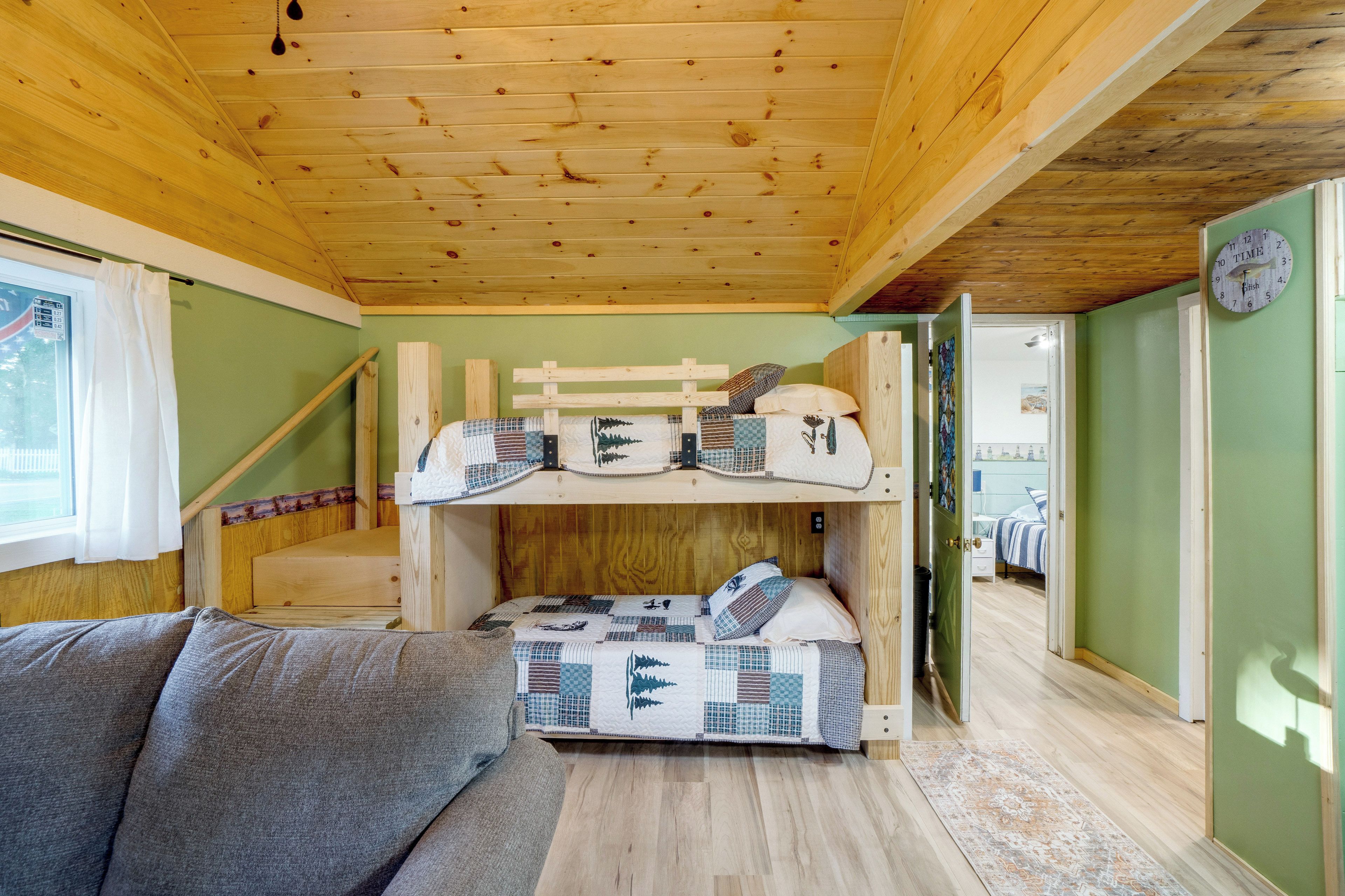 A bunk bed room with a wooden ceiling, a window with curtains, and a green wall.