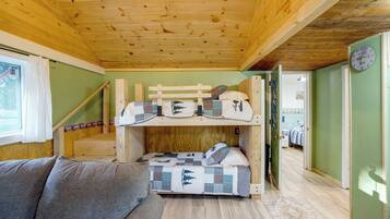 A bunk bed room with a wooden ceiling, a window with curtains, and a green wall.