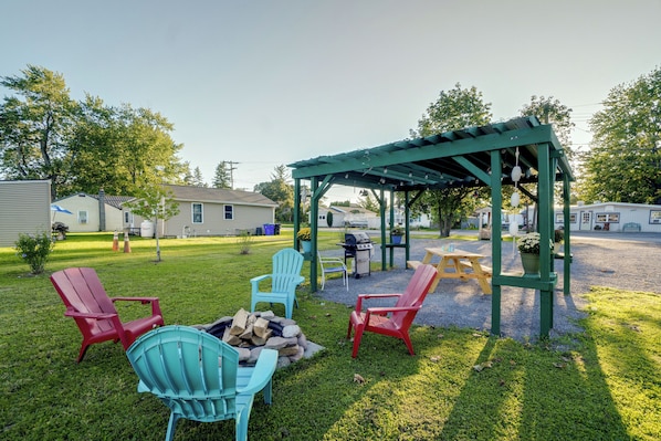 A backyard with a wooden pergola, outdoor seating, and a fire pit. - Walk to Lake Ontario! 'minnow Cottage' (Kent)