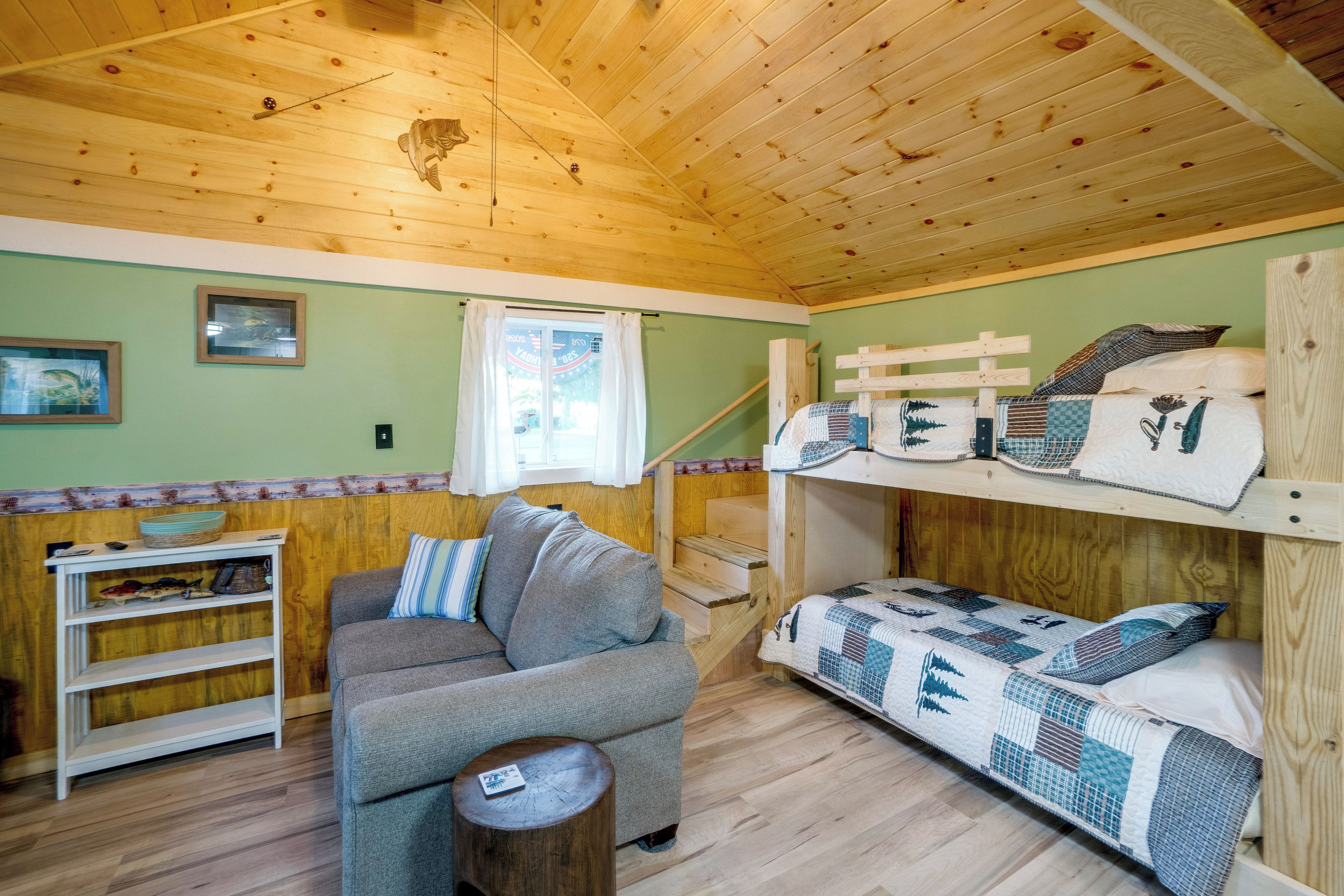 A cozy cabin interior with a wooden ceiling, a sofa, a bunk bed, and a small table.