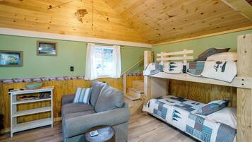 A cozy cabin interior with a wooden ceiling, a sofa, a bunk bed, and a small table.
