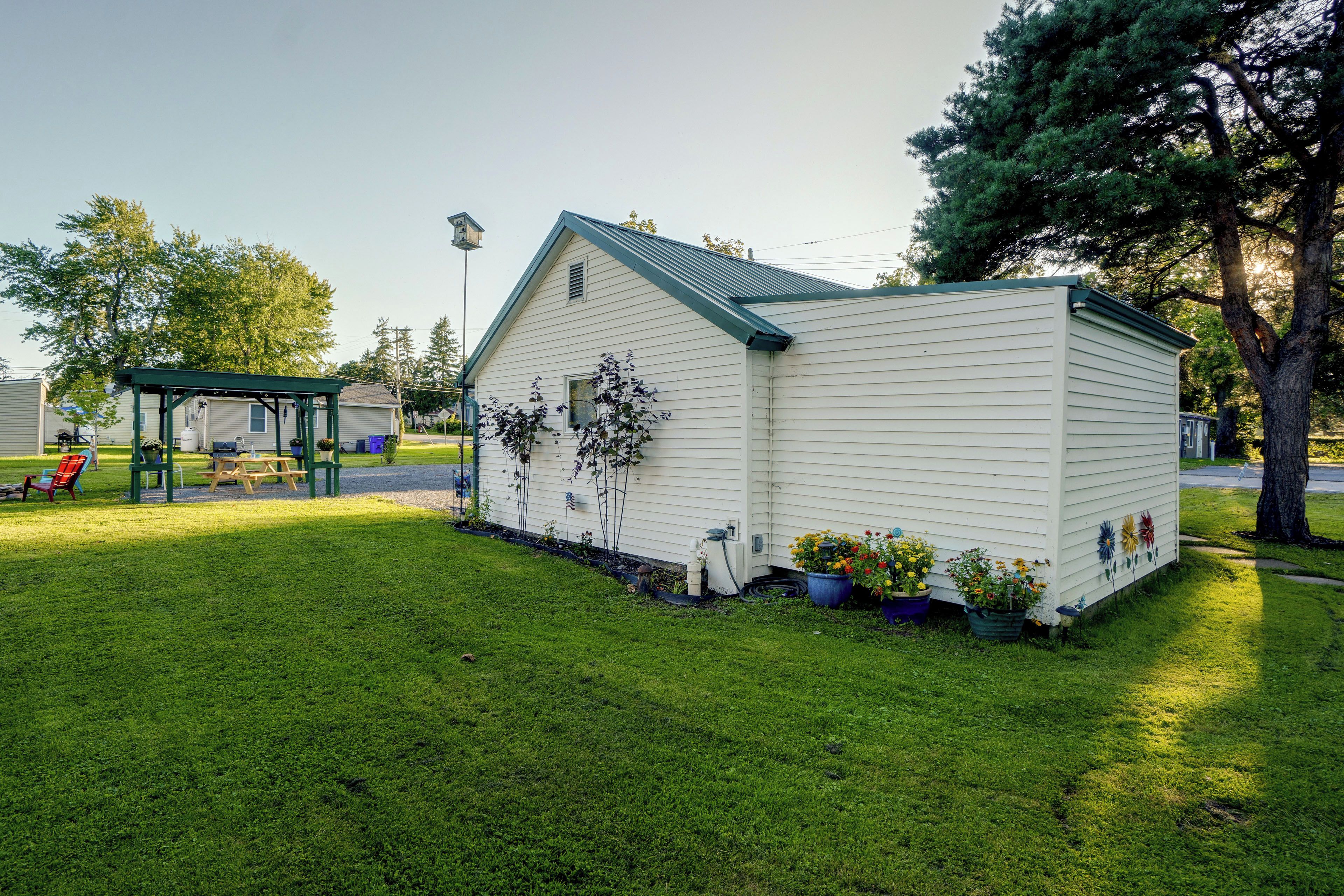 A small, single-story house with a green roof and white siding, surrounded by a well-maintained lawn and potted plants.