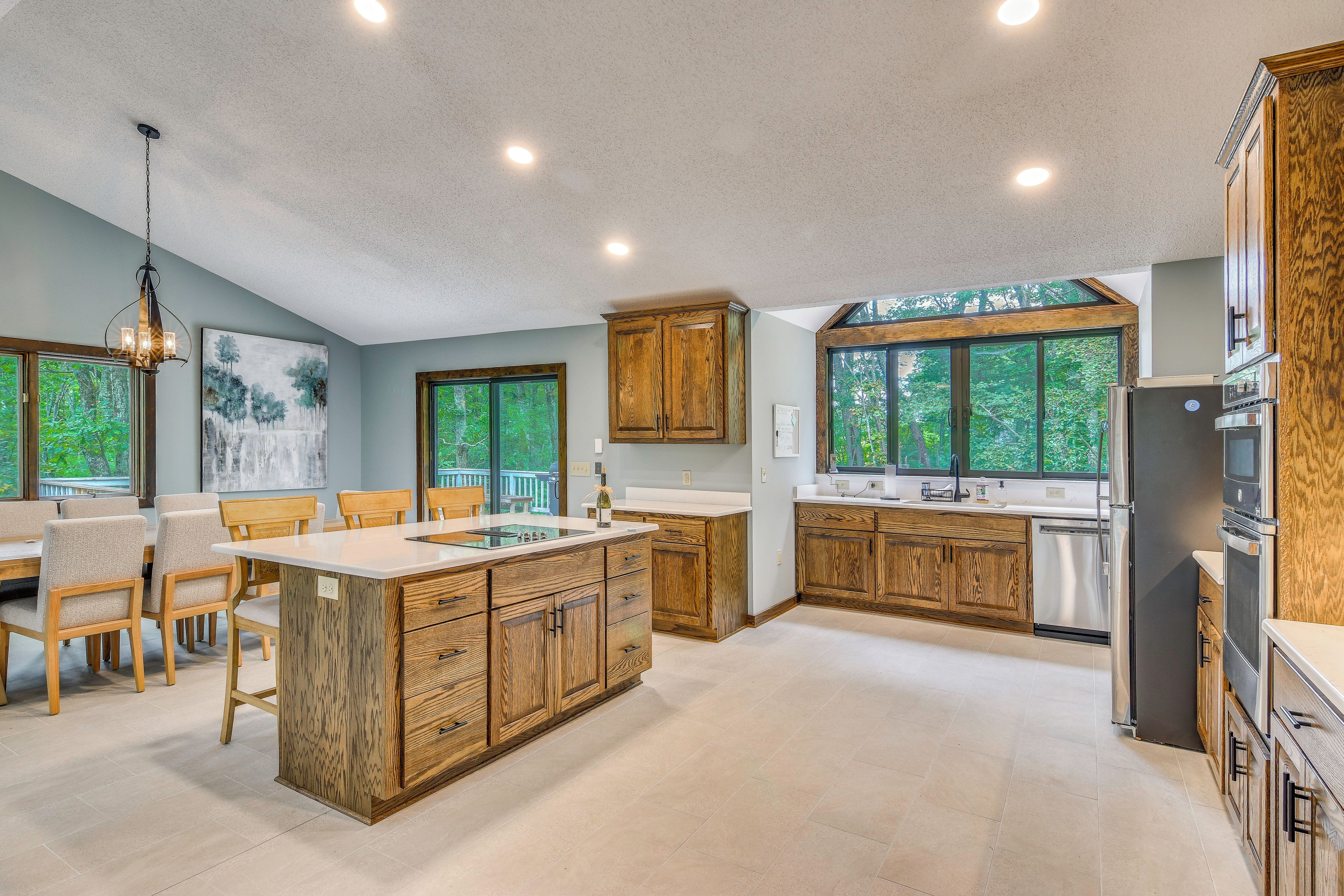 A modern kitchen with wooden cabinets, a central island, and large windows.
