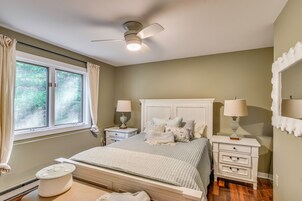 Un dormitorio con cama, mesitas de noche, ventilador de techo y una ventana con cortinas.