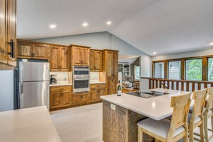 A kitchen with wooden cabinets, stainless steel appliances, a large island with chairs, and a view of a balcony.