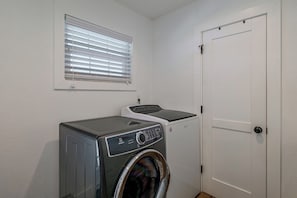 A laundry room with a front-loading washer and dryer, a window with blinds, and a white door. - Winter Haven Chain of Lakes Getaway Near Legoland (Winter Haven)