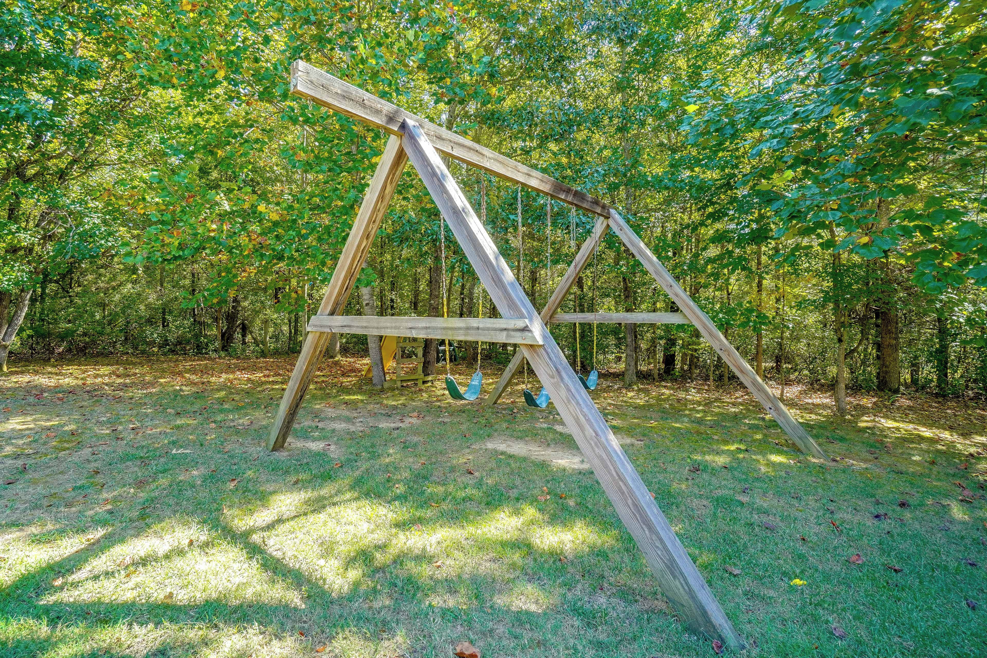 A wooden swing set in a grassy area with trees in the background.