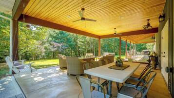 An outdoor covered patio with a table and chairs, a swing, and a view of a garden.