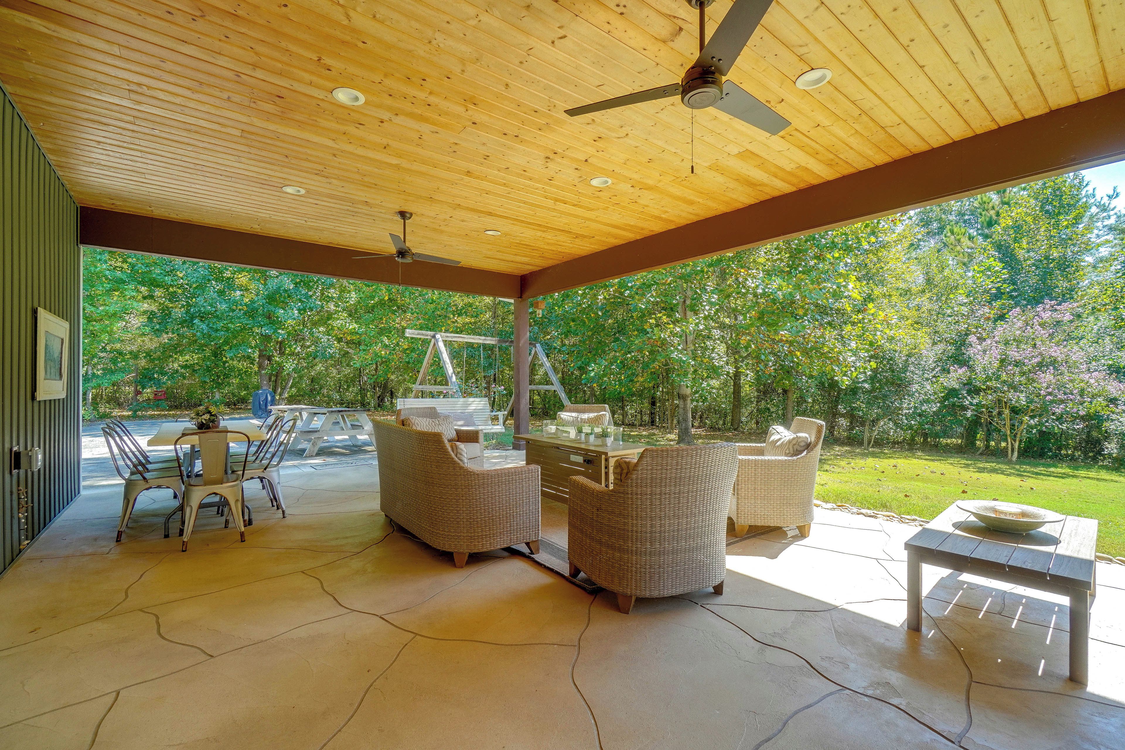 A covered patio with outdoor furniture, a ceiling fan, and a view of a wooded area.
