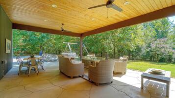 A covered patio with outdoor furniture, a ceiling fan, and a view of a wooded area.