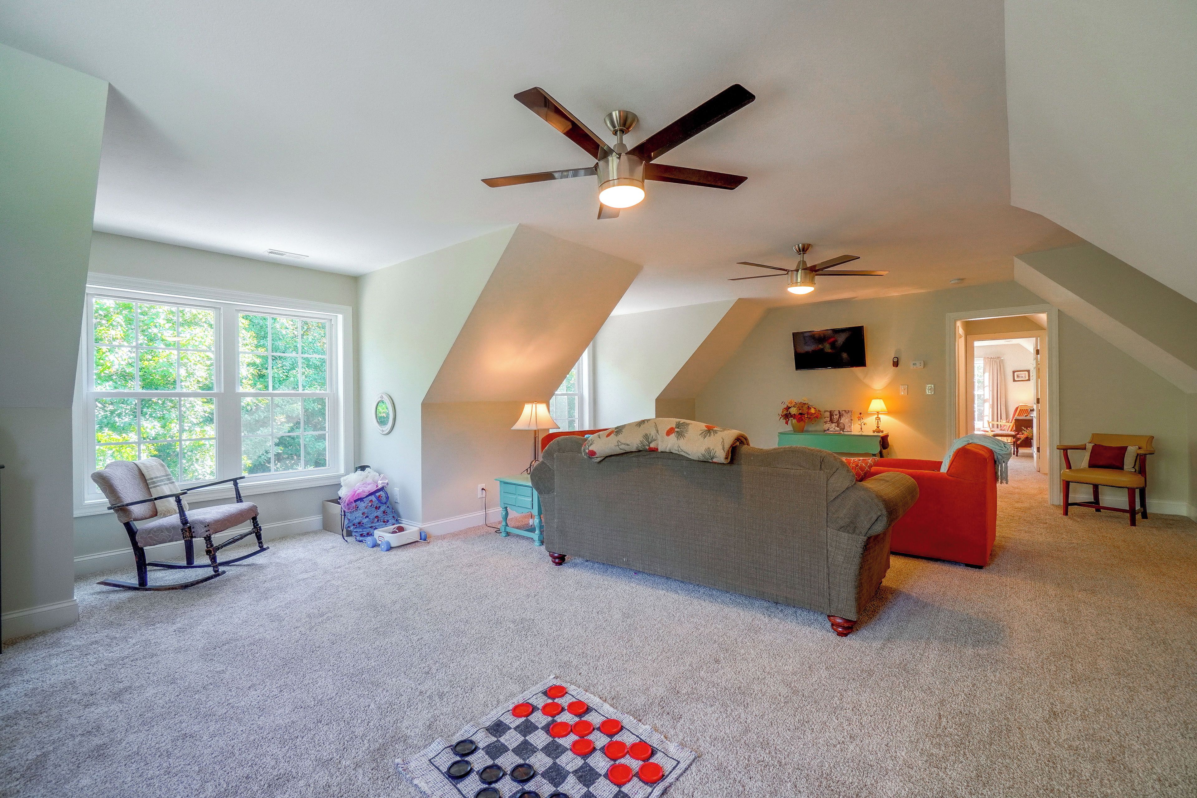 A spacious attic bedroom with a sloped ceiling, a ceiling fan, and a large window providing natural light.