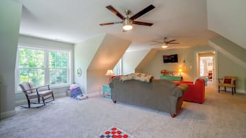 A spacious attic bedroom with a sloped ceiling, a ceiling fan, and a large window providing natural light.