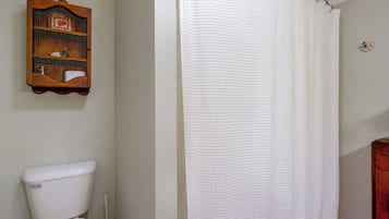 A bathroom with a toilet, a shower curtain, and a wooden cabinet with a picture frame.