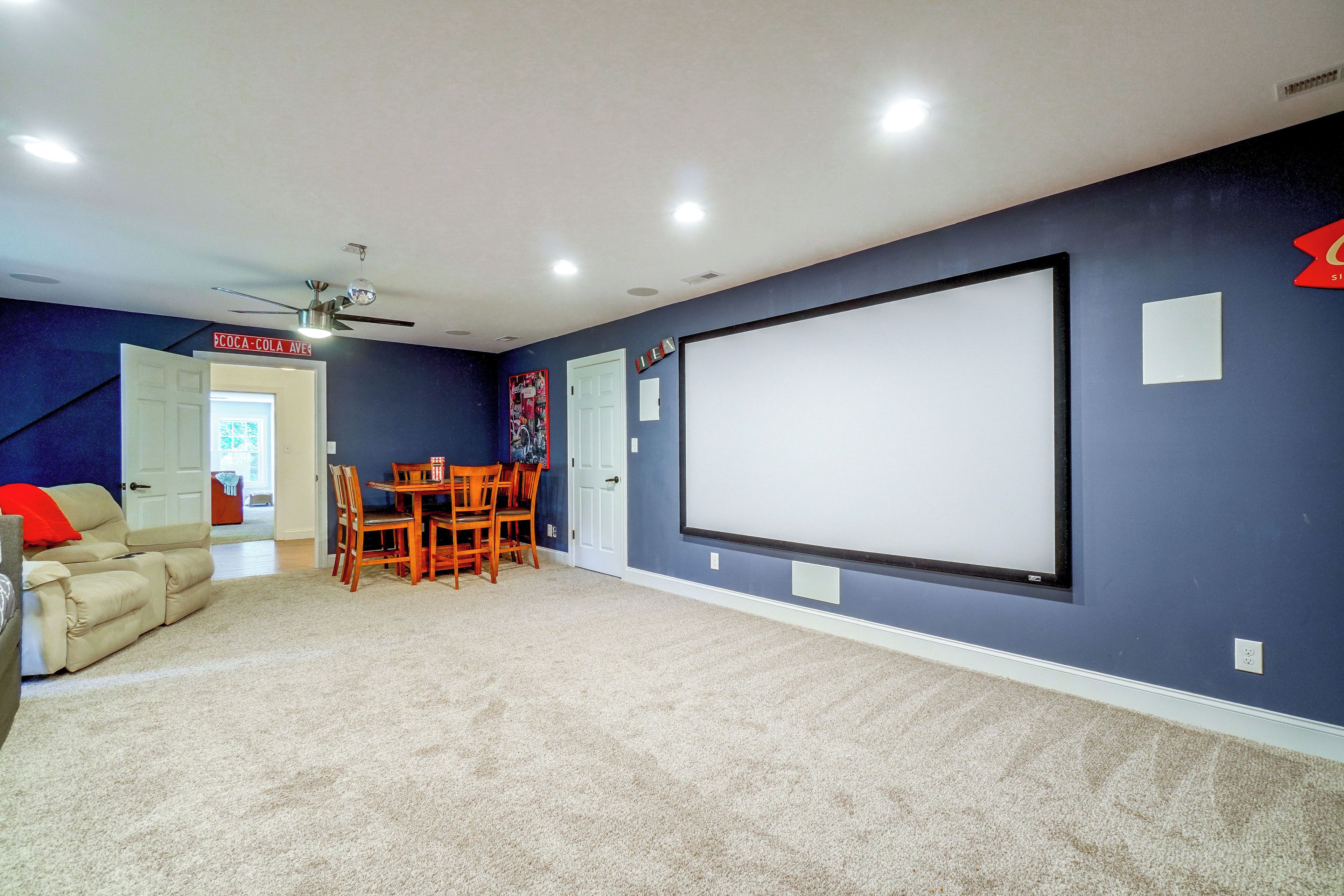 Sala de cine en casa con pantalla grande, ventilador de techo y zona de estar.