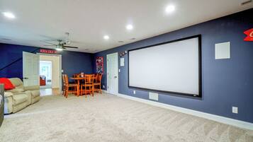 Sala de cine en casa con pantalla grande, ventilador de techo y zona de estar.